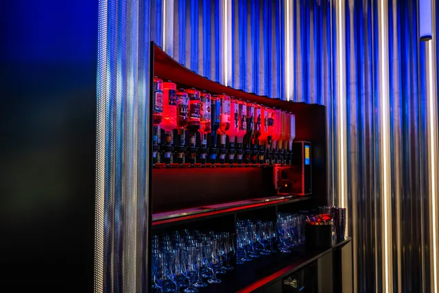 CocktailBot hinter der Theke mit roter und blauer Lichtshow, darunter Gläser