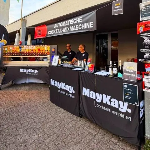 MayKay-Stand mit automatischer Cocktail-Mixmaschine, zwei Personen hinter der Theke